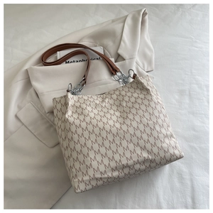 Dettaglio flat lay della borsa tote beige con stampa a M e manici in pelle catena