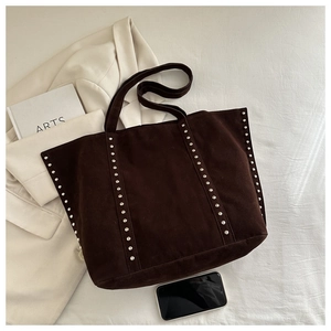 Flat lay of brown suede tote bag with silver rivets, light suit and artsy book props