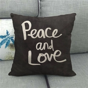 Black linen throw pillow with white Peace and Love text on a grey fabric sofa