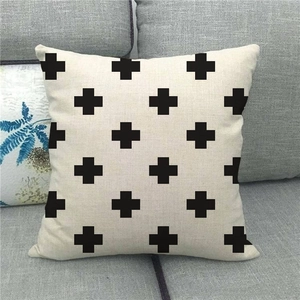 Close-up of beige linen pillow cover featuring symmetrical black cross patterns on grey sofa