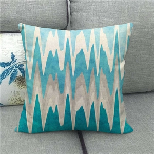 Linen cushion cover with teal and blue geometric zigzag pattern on a grey sofa