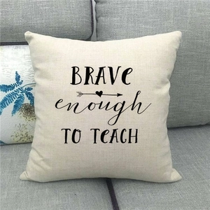 Close-up of linen pillow cover with Brave enough TO TEACH quote on grey sofa