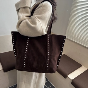 Large dark brown suede tote bag with stylish silver rivets shown on a model in a minimalist room