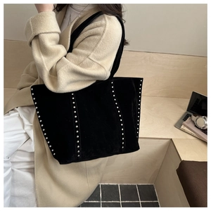 Detail of black suede tote bag featuring vertical silver studs and a laptop in a city setting
