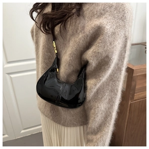 Detail of glossy black patent leather crescent bag with elegant gold metal strap accents
