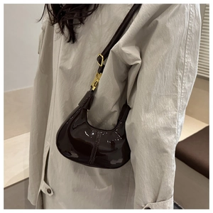 Detail of dark brown patent leather crescent bag with gold metallic buckle and glossy finish