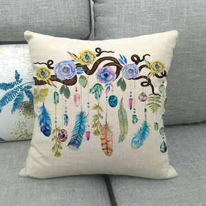 Fodera per cuscino in lino con ghirlanda floreale e piume boho su un divano grigio sobrio