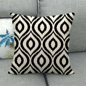 Modern black and white geometric ikat linen cushion cover on a gray fabric sofa