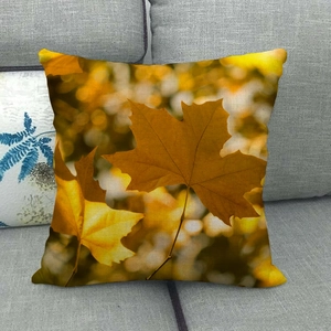 Linen autumn throw pillow case with painted maple leaves on a grey fabric sofa
