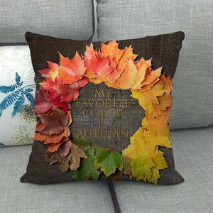 Close-up of linen pillow cover with maple leaf wreath and autumn text on a sofa