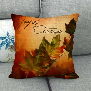 Close-up of linen pillowcase with autumn maple leaves and Joy of Autumn text on gray sofa