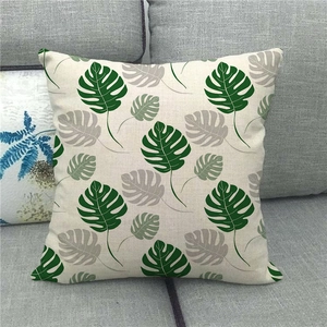 Square linen pillowcase with monstera leaf pattern on a grey fabric sofa background