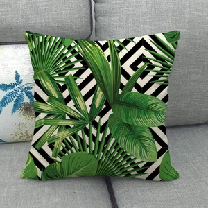 Detail of linen pillowcase with tropical green leaves and black stripes on a sofa