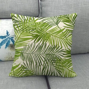 Linen square pillowcase with green tropical palm leaf print on a gray sofa
