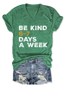 Flat lay of a green V-neck T-shirt with Be Kind slogan and distressed denim shorts