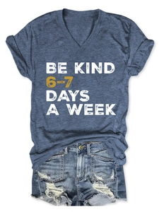 Detail of Be Kind slogan print on V-neck navy T-shirt paired with distressed denim shorts