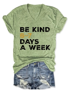 Flat lay of green V-neck T-shirt with 'Be Kind' slogan and distressed denim shorts