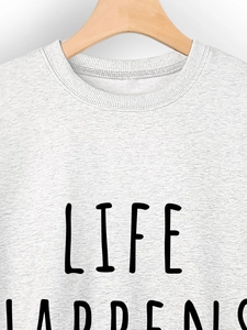 Close-up of LIFE HAPPENS slogan printed on light gray crewneck sweatshirt fabric