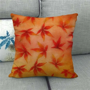 Detail of linen autumn pillow cover with red maple leaf pattern on a grey fabric sofa