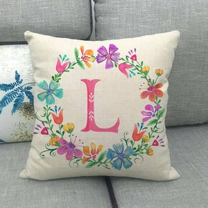 Federa in lino con ghirlanda floreale e lettera L rosa su un divano in tessuto grigio
