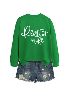 Detail of green Realtor Life sweatshirt paired with distressed denim shorts on white background