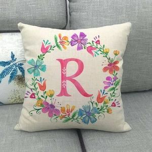 Fodera per cuscino in lino con ghirlanda floreale e lettera rosa R su divano grigio