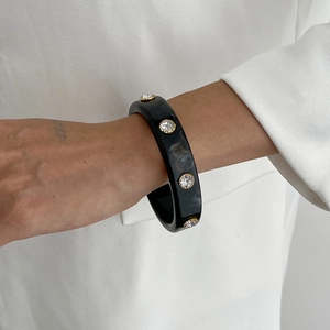 Dettaglio del bracciale rigido in resina nera marmorizzata con cristalli dorati su modella