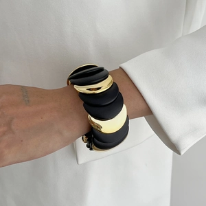 Dettaglio di bracciale rigido con dischi alternati in nero opaco e finitura oro lucido