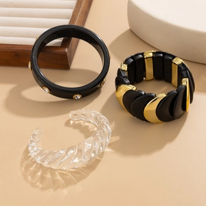 Dettaglio del set di bracciali in resina nera, metallo dorato e acrilico intrecciato