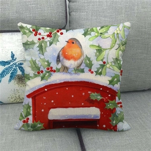 Housse de coussin en lin avec oiseau rouge-gorge aquarelle et baies de houx sur un canapé