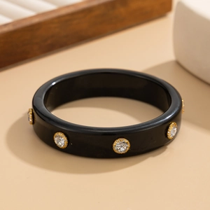 Dettaglio macro del bracciale in resina nera con strass bordati d'oro in stile elegante