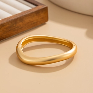 Detail view of a gold irregular wavy bangle with a matte finish on a jewelry box