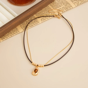 Detail of layered gold necklace featuring a teardrop tiger eye pendant on a vintage background
