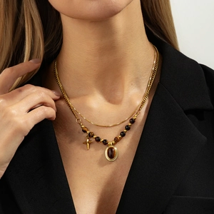Double-layered gold necklace with tiger eye beads and cross pendant on a model