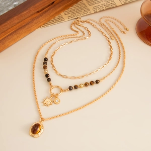 Detail of layered gold necklace with tiger eye stone and sun charm on vintage background