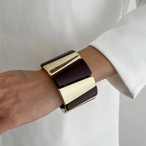 Détail d'un large bracelet géométrique en métal doré poli et empiècements marron foncé