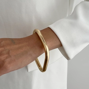 Close-up of irregular chunky gold wavy bangle worn on wrist with minimalist white clothing