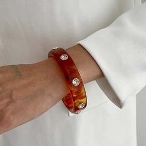 Détail du bracelet en résine ambre avec cristaux blancs sur manche de veste blanche