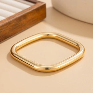 Macro detail of polished gold square bangle with smooth thick edges on a warm display