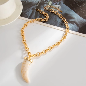 Fashion gold chain necklace featuring a cream resin horn pendant on a minimalist desk