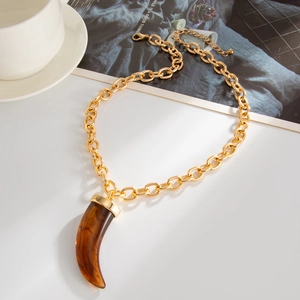 Ethnic style necklace with golden chain and amber resin tusk pendant on white surface