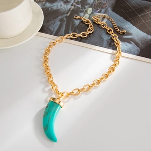 Detailed view of bohemian turquoise horn pendant with gold chain on a minimalist table