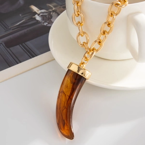 Detail of amber marble resin tusk pendant with gold chunky chain on a white cup
