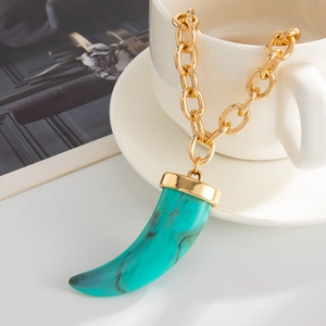 Detail of bohemian gold link chain with a teal marbled resin horn pendant on a white cup