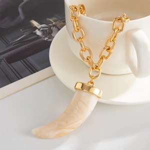 Close-up of gold chain necklace with marbled resin horn pendant on white porcelain cup