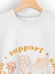 Close-up of light gray sweatshirt featuring orange SUPPORT text and floral prints