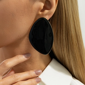 Close-up of a model wearing large irregular black resin earrings with gold-plated trim