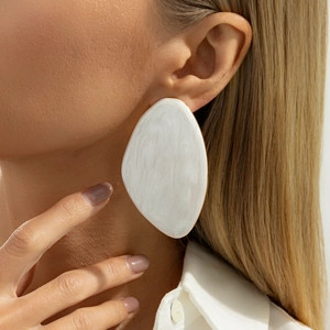 Detail of large teardrop earrings with white marble texture and gold metal edges on model