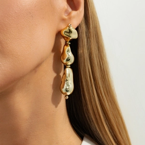 Close-up of gold irregular geometric teardrop tassel earrings worn by a model