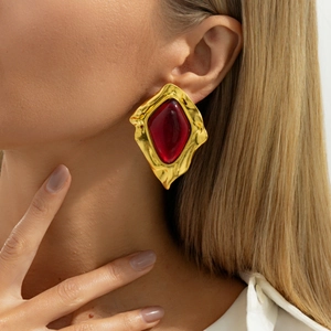 Detail shot of vintage gold earrings with hammered metal and a large red gemstone